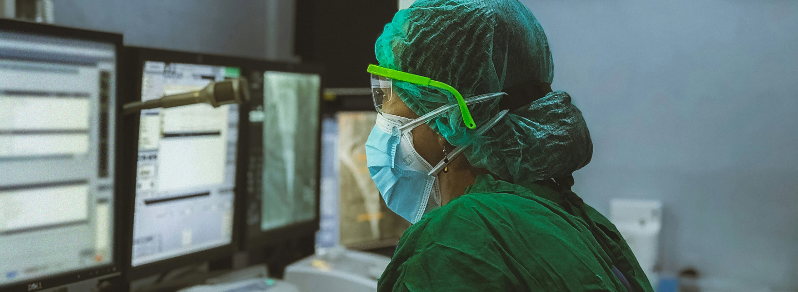 A female doctor wearing a mask, reviewing reports on a computer